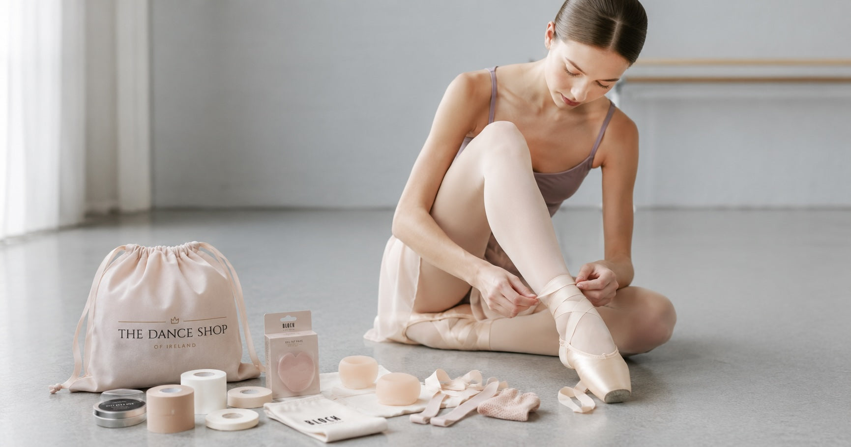 Young ballet dancer preparing her pointe shoes in a dance studio with toe pads, ribbons and pointe shoe accessories beside her.