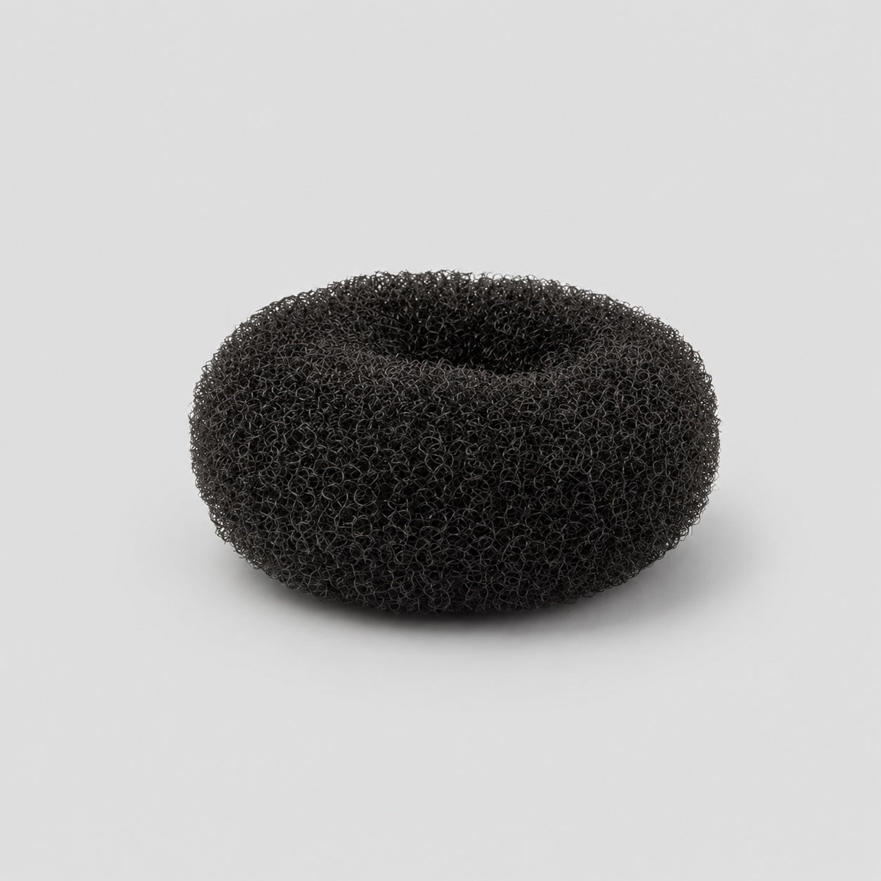 Side profile view of black ballet bun doughnut hair accessory on light grey background