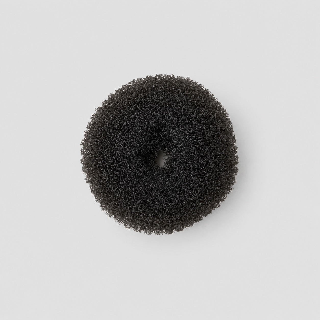 Top view of black ballet bun doughnut hair accessory on light grey background