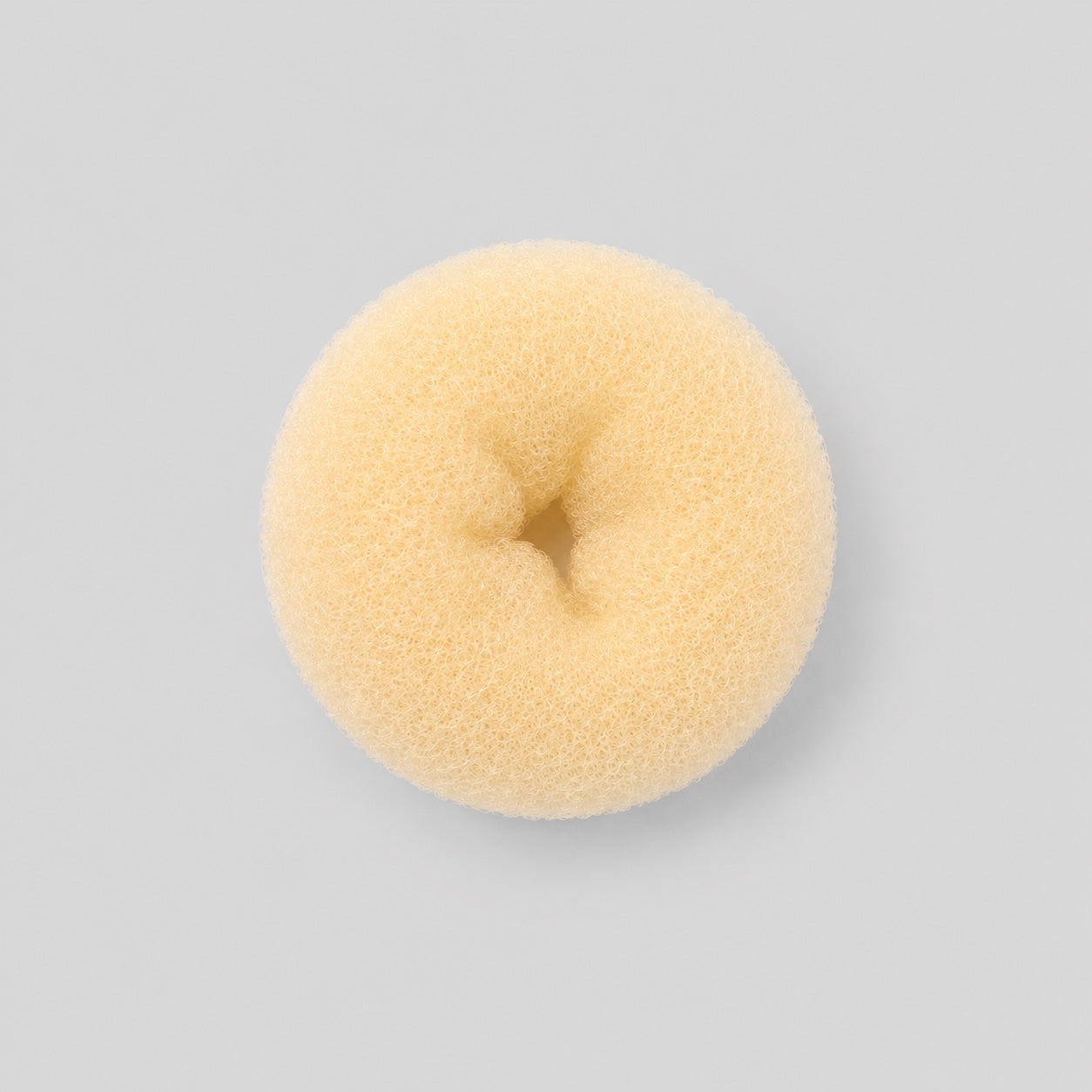 Bottom view of blonde ballet bun doughnut hair accessory on light grey background