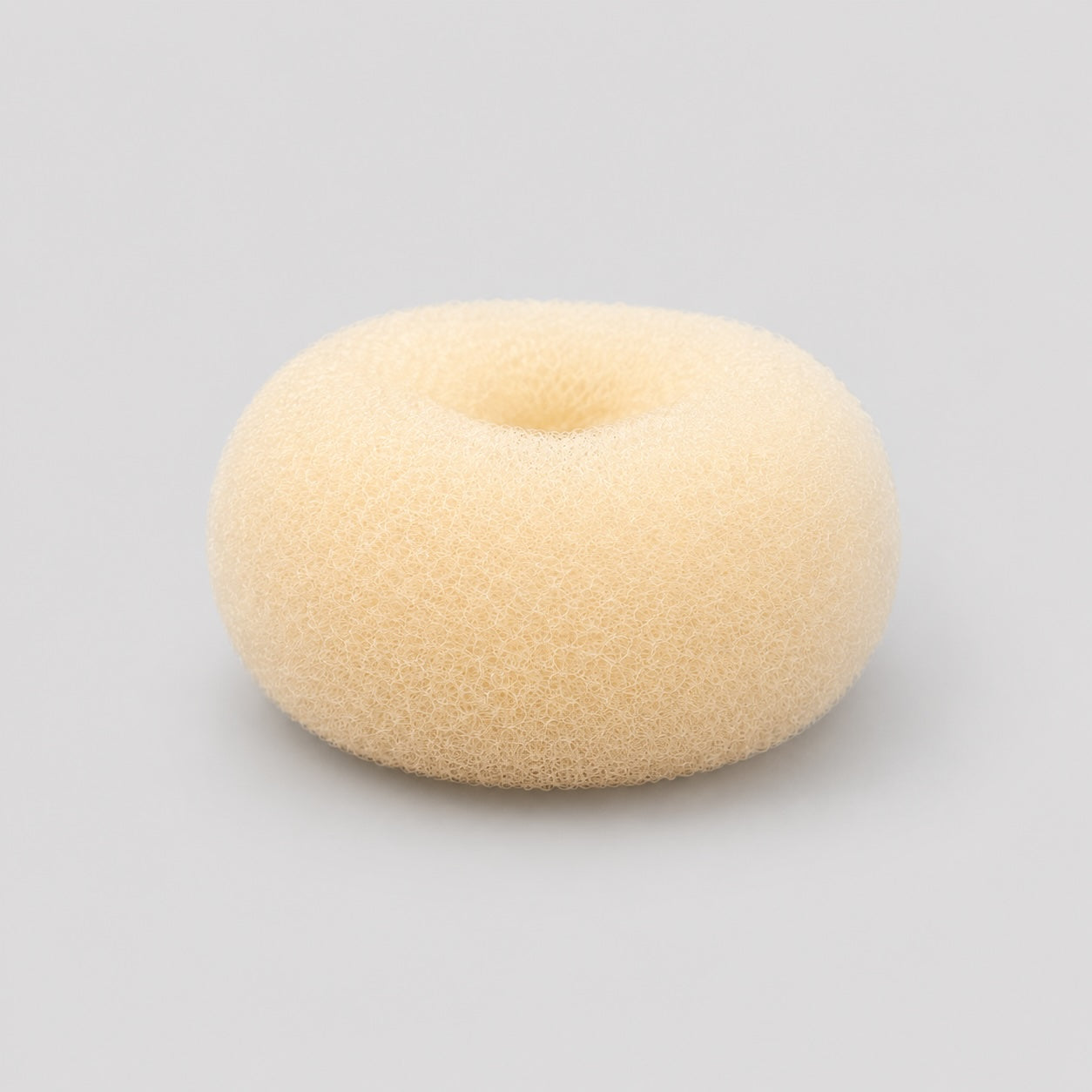 Side profile view of blonde ballet bun doughnut hair accessory on light grey background