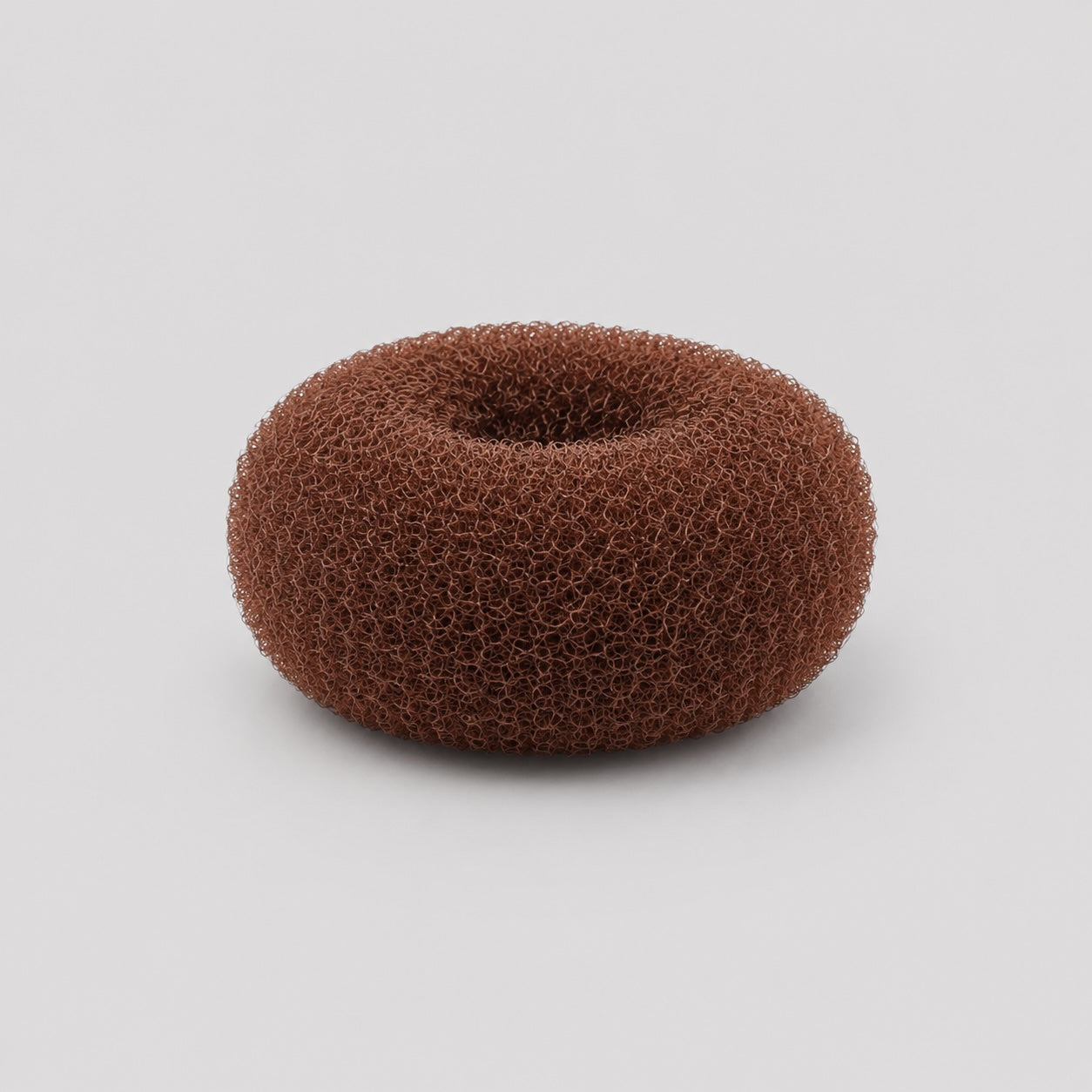 Side profile view of brown ballet bun doughnut hair accessory on light grey background