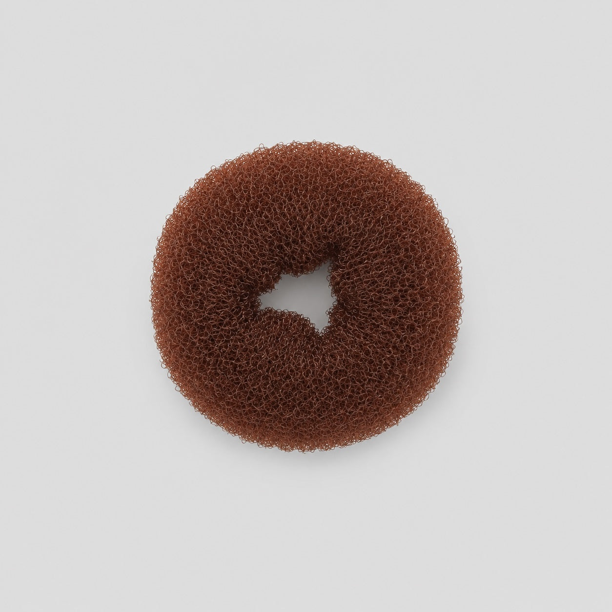 Top view of brown ballet bun doughnut hair accessory on light grey background