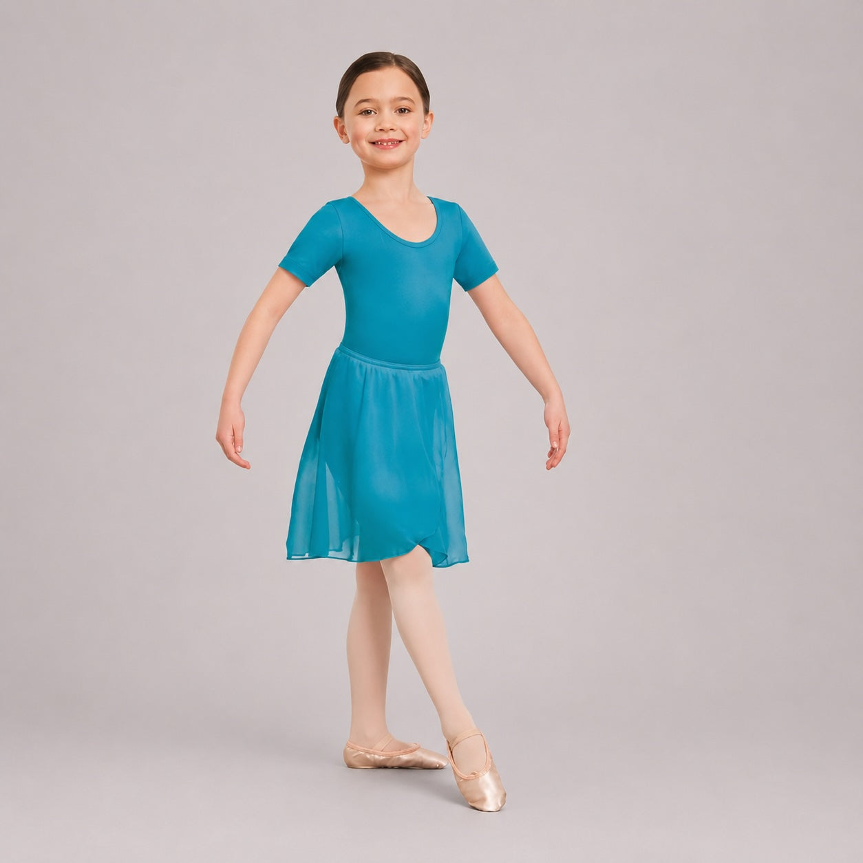 Girl wearing a marine chiffon ballet wrap skirt by 1st Position over a teal ballet leotard on a light grey studio background.