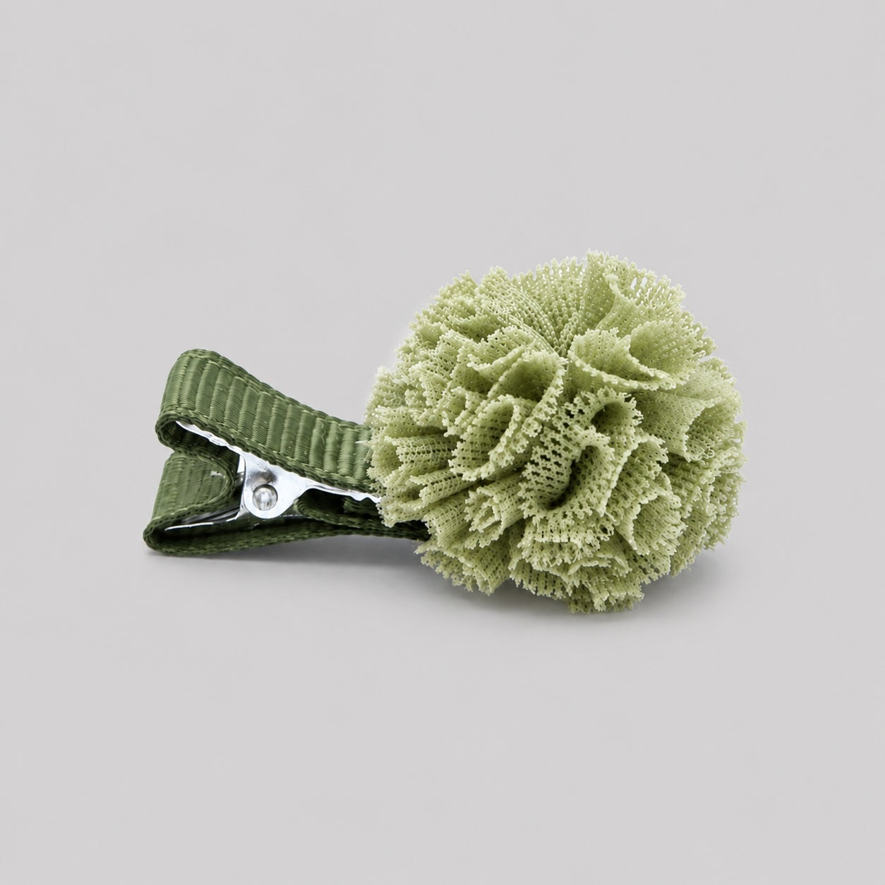 Green pom pom hair clip with textured fabric flower on a light grey background for dancers and girls hair accessories