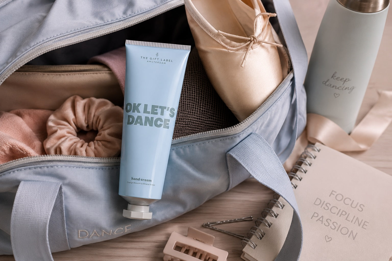 Blue OK Let’s Dance hand and body cream styled inside a dancer’s ballet bag with ballet shoes and dance accessories.