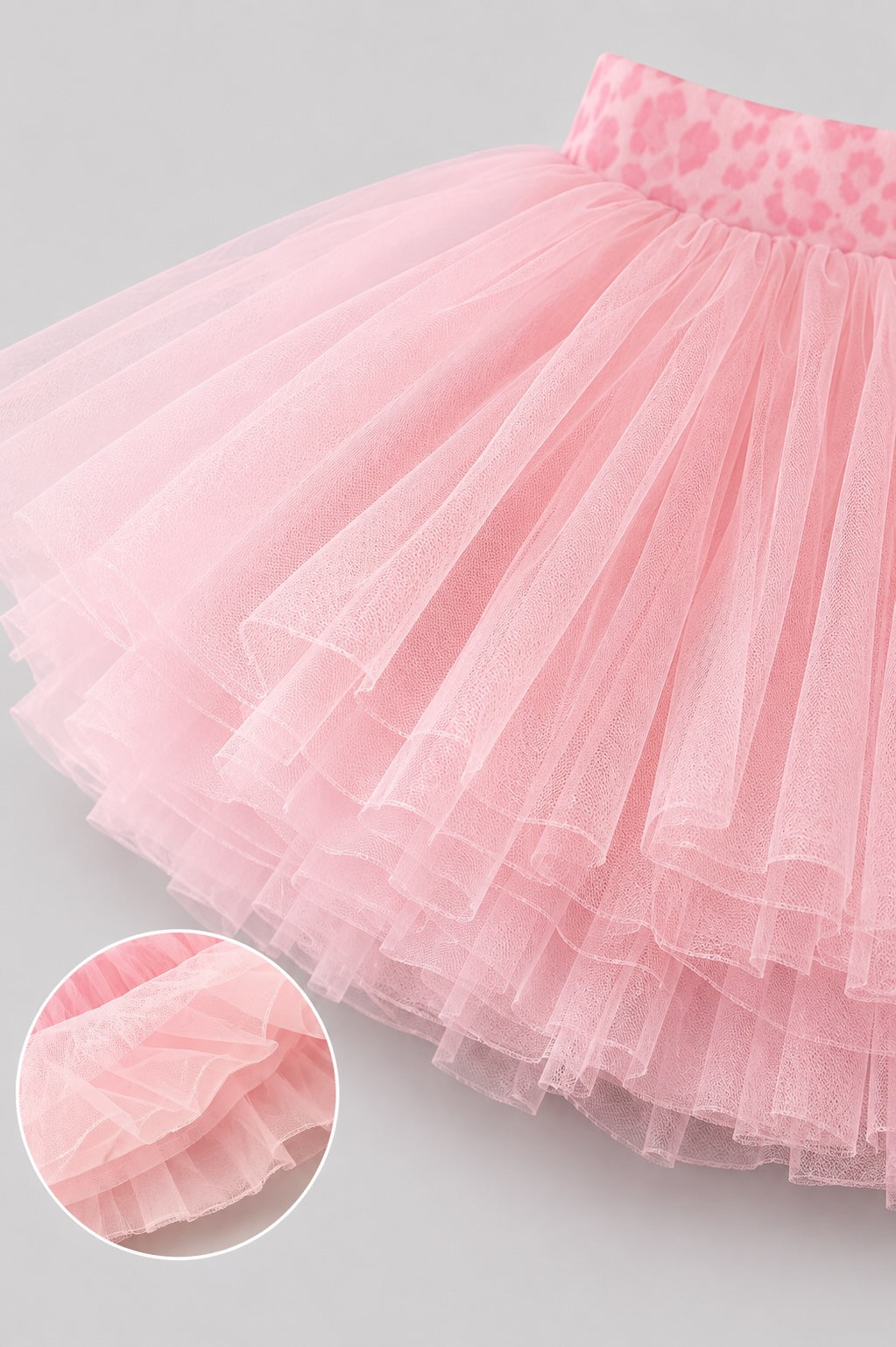 Close-up detail of layered soft pink ballet tutu skirt showing fluffy tulle layers and waistband on a light grey background