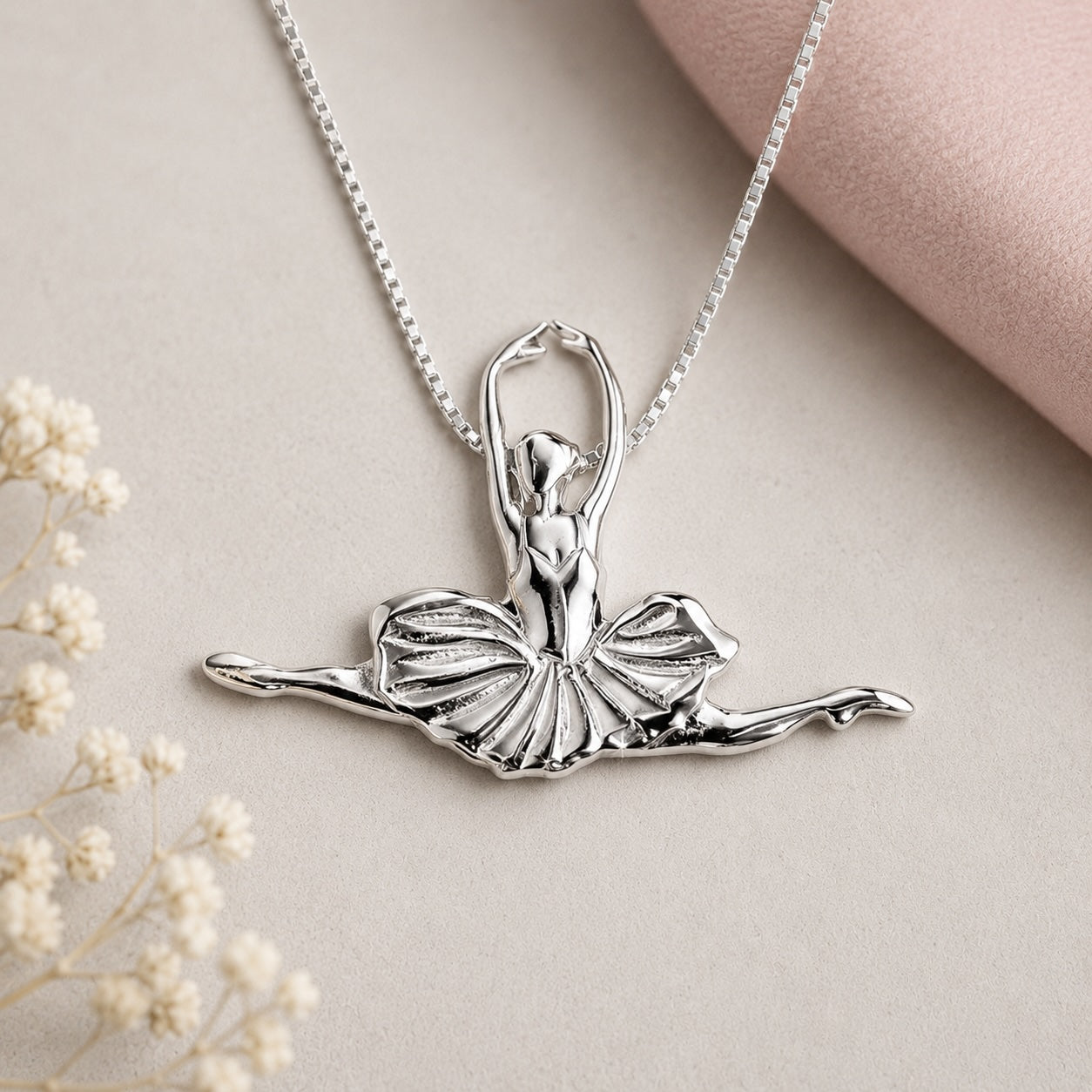 Silver ballerina pendant necklace in seated ballet pose on a soft neutral background with delicate floral styling.